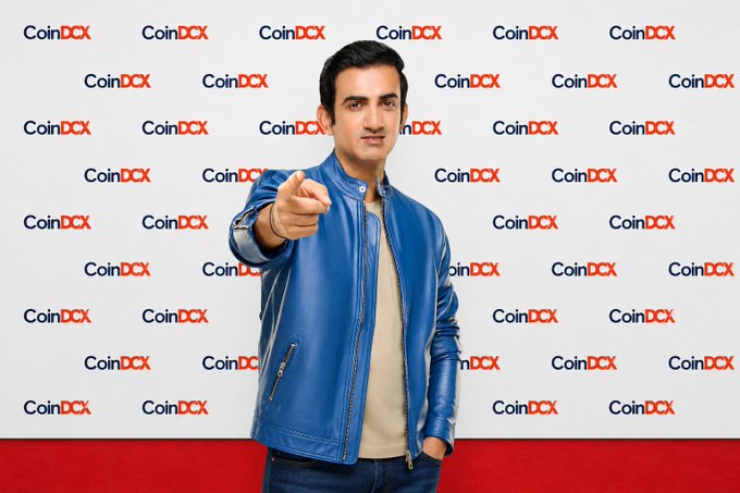A man in a blue leather jacket points directly at the camera while standing in front of a step-and-repeat backdrop featuring the "CoinDCX" logo repeated in blue and red. The promotional-style photo accompanies a post introducing CoinDCX as one of India's leading cryptocurrency exchanges, founded in 2018.