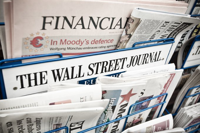 A close-up of a newspaper stand displaying copies of "THE WALL STREET JOURNAL" and "FINANCIAL TIMES," the latter with an article titled "In Moody's defence" by Wolfgang Münchau.