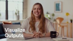 A woman smiles while sitting at a table in a bright room with the text 'Visualize Outputs' overlaid on the image.