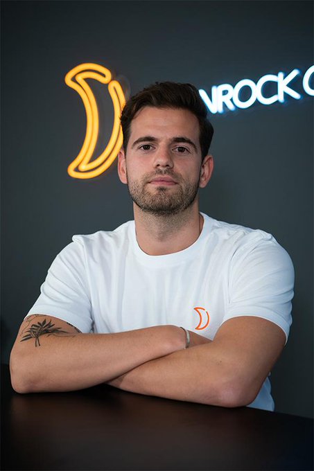 A man in a white t-shirt with arms crossed sits at a dark table in front of a neon "LIVROCK" sign and logo, projecting a polished, professional vibe that visually signals the career transition described in the caption.