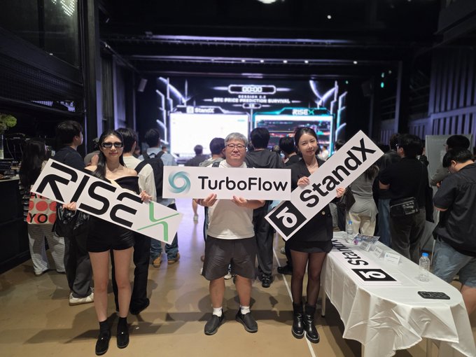 A promotional photo from a tech event in Seoul, Korea showing three people holding signs for 'RISEX', 'TurboFlow', and 'StandX' with a '2025 SEOUL SUMMIT' screen in the background.