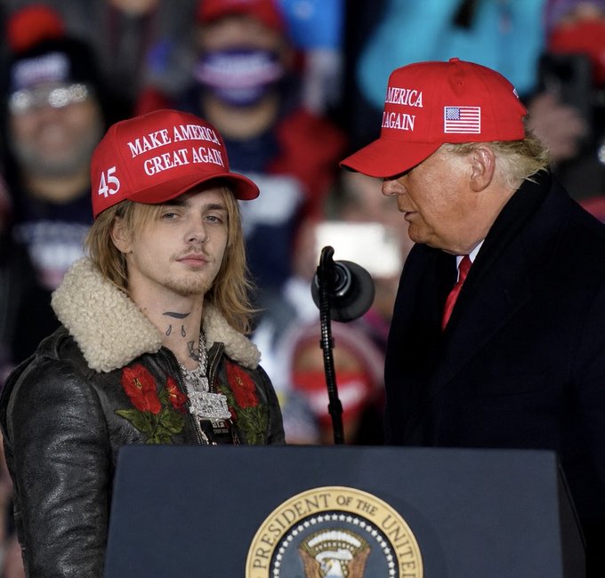 Musician Justin Bieber, wearing a red 'Make America Great Again' cap, stands at a presidential podium alongside Donald Trump, who also wears a red 'America Again' cap.