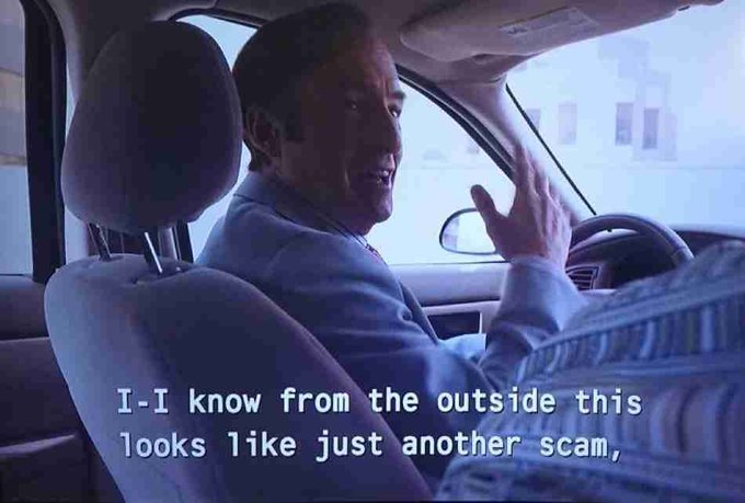 A man in a suit sits in a car, gesturing as he speaks, with the subtitle reading "I-I know from the outside this looks like just another scam," humorously matching the post about defensively explaining purchases to his wife.
