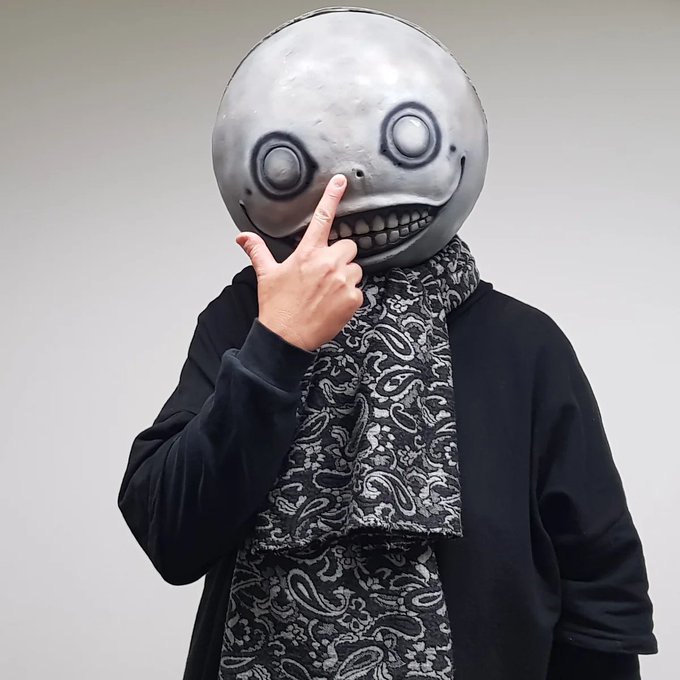 The image shows a person wearing a creepy, smiling grey mask with hollow eyes and a wide grin, paired with a black outfit and a black-and-white paisley scarf, while holding up a middle finger. The masked, anonymous figure with a defiant gesture fits the post's rebellious tone of shilling a tool to new followers, embodying the irreverent and edgy crypto/Twitter culture vibe.