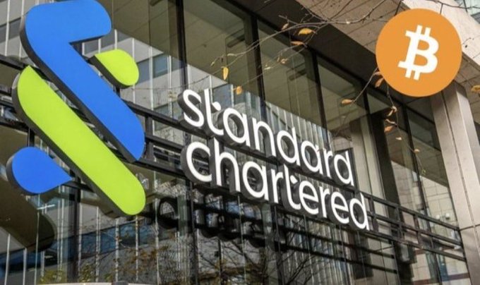 The image shows the Standard Chartered bank logo and signage on a building exterior, with a Bitcoin (₿) symbol in the upper right corner, visually connecting the traditional banking giant to the cryptocurrency space as the post announces Standard Chartered's launch of spot BTC and ETH trading for institutional clients in the UAE.