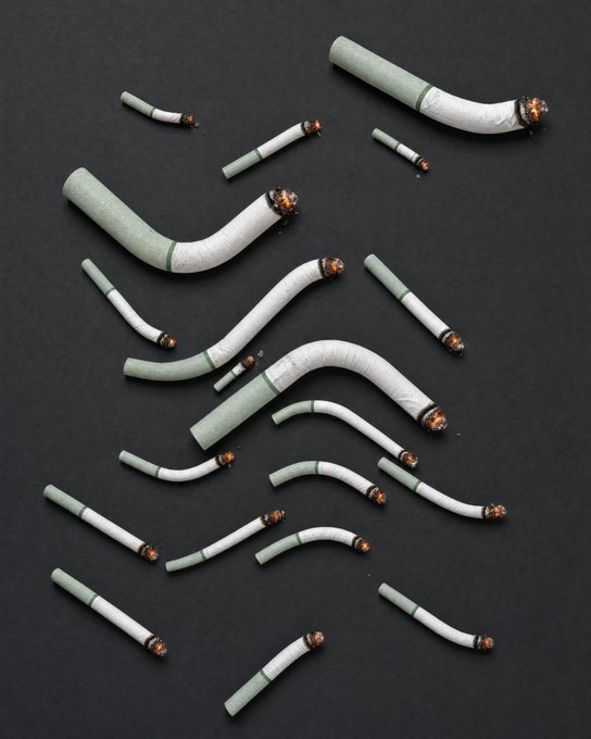 Multiple crushed and bent cigarettes scattered across a black surface, with greenish-white filters and burnt orange tips.