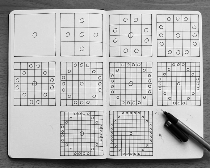 A sketchbook open on a wooden surface showing hand-drawn grid patterns with circles at the intersections, progressively increasing in complexity, with a black marker resting on the page.
