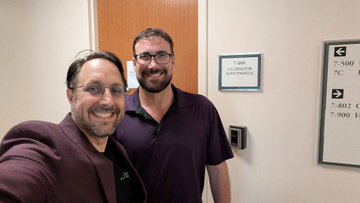 Two men pose for a selfie outside what appears to be Senator Padilla's California field office, with a visible directory sign listing room numbers "7-500, 7-502, 7-900" and an office hours placard. The image accompanies a message thanking the team for advocating on behalf of the CLARITY Act, showing the advocates at the location where they made their case for clear crypto regulations.