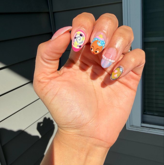 A hand displays detailed nail art featuring pastel colors, smiley faces, and a cute cartoon character on one nail.