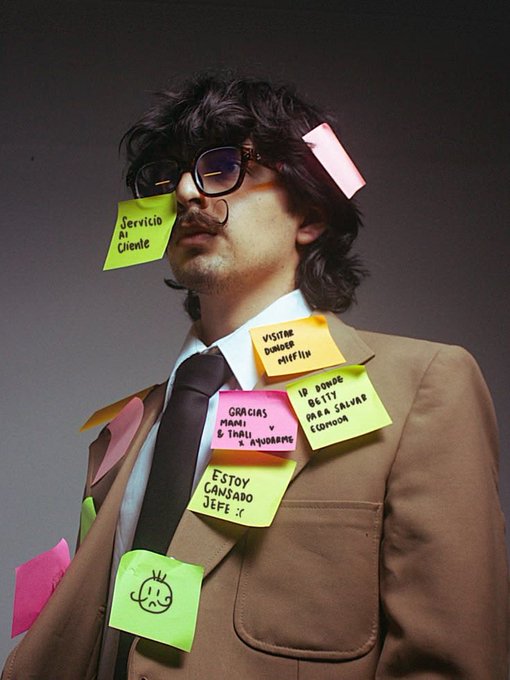 A man in a brown suit and glasses covered in colorful sticky notes with Spanish phrases like 'Servicio Al Cliente', 'Visita Danger Muffin', and 'Estoy Cansado Jefe'.