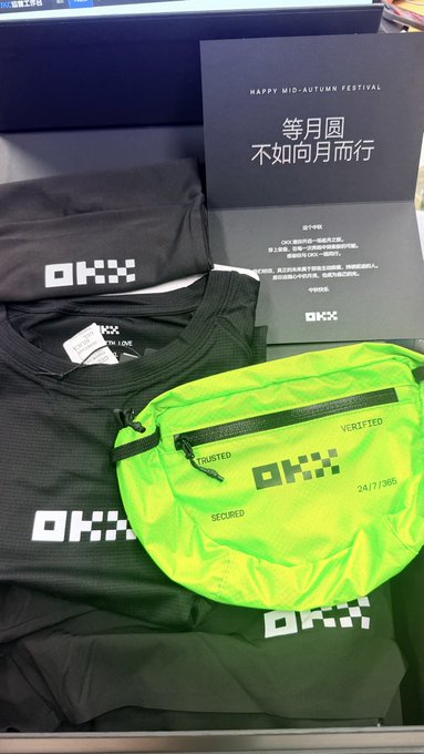 An OKX Mid-Autumn Festival gift box containing black OKX-branded clothing and a neon green OKX fanny pack, with a card reading 'HAPPY MID-AUTUMN FESTIVAL 等月圆 不如向月而行' (limited to 241/7,300).