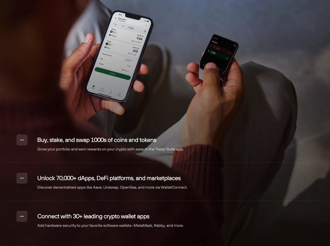 The image shows a person holding two cell phones with their hands, one of which displays a screen showing a cryptocurrency exchange page. The other phone has an app icon that says "Unlock your wallet" along with some text about hardware wallets. The background is blurred and appears to be a room or a street.