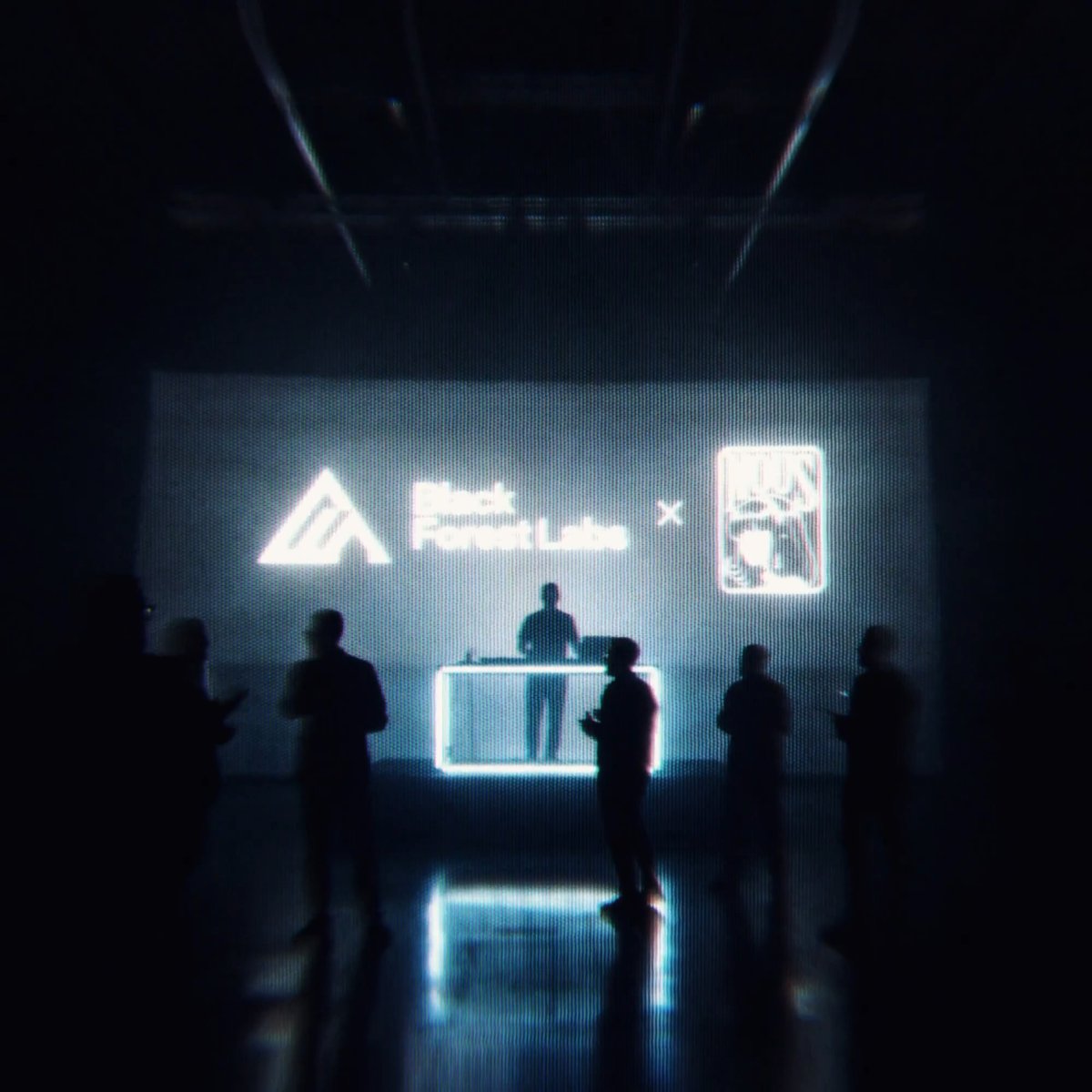 Silhouetted figures gather in a dimly lit venue where a large screen displays a glowing collaboration graphic featuring the Adidas logo alongside the word "FluxLab" and an "×" symbol beside a stylized emblem, mirroring the user's hint of a "Hermes + Flux3?" partnership teaser.