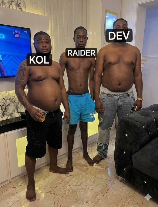 Three shirtless friends—labeled "KOL," "RAIDER," and "DEV"—stand side by side in a living room, with the outer two holding drinks and the noticeably slimmer middle friend (RAIDER) standing between them, playing into the "who did this" caption as a humorous comparison of body types.