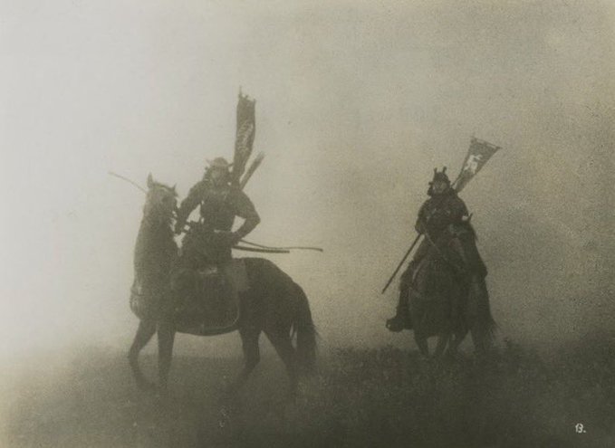 The image depicts two people riding horses, possibly samurai warriors or samurais from a historical era. The riders are wearing armor and holding swords, which suggests that they might be engaged in combat or participating in a reenactment of a historical event. The scene is set against a foggy background, adding to the atmosphere of the image.