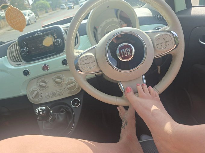 Interior view of a mint-colored Fiat car showing the steering wheel with Fiat logo, dashboard, and a person's hand resting on the wheel while another is on the gear shift.