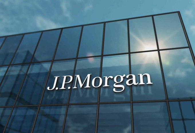 The J.P.Morgan logo displayed on a glass office building facade with sun glare reflecting off the windows.