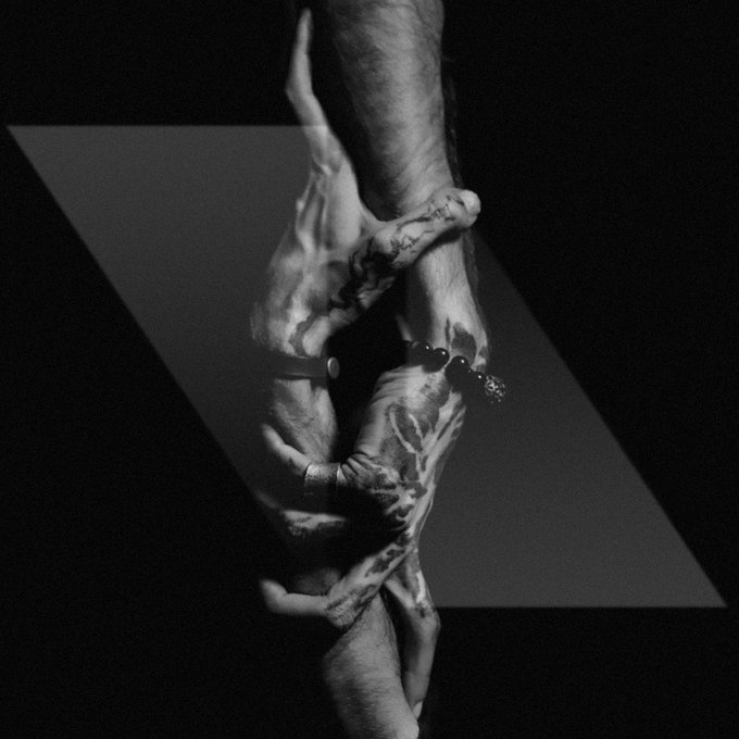 A black and white artistic photograph shows intertwined hands against a dark geometric background.