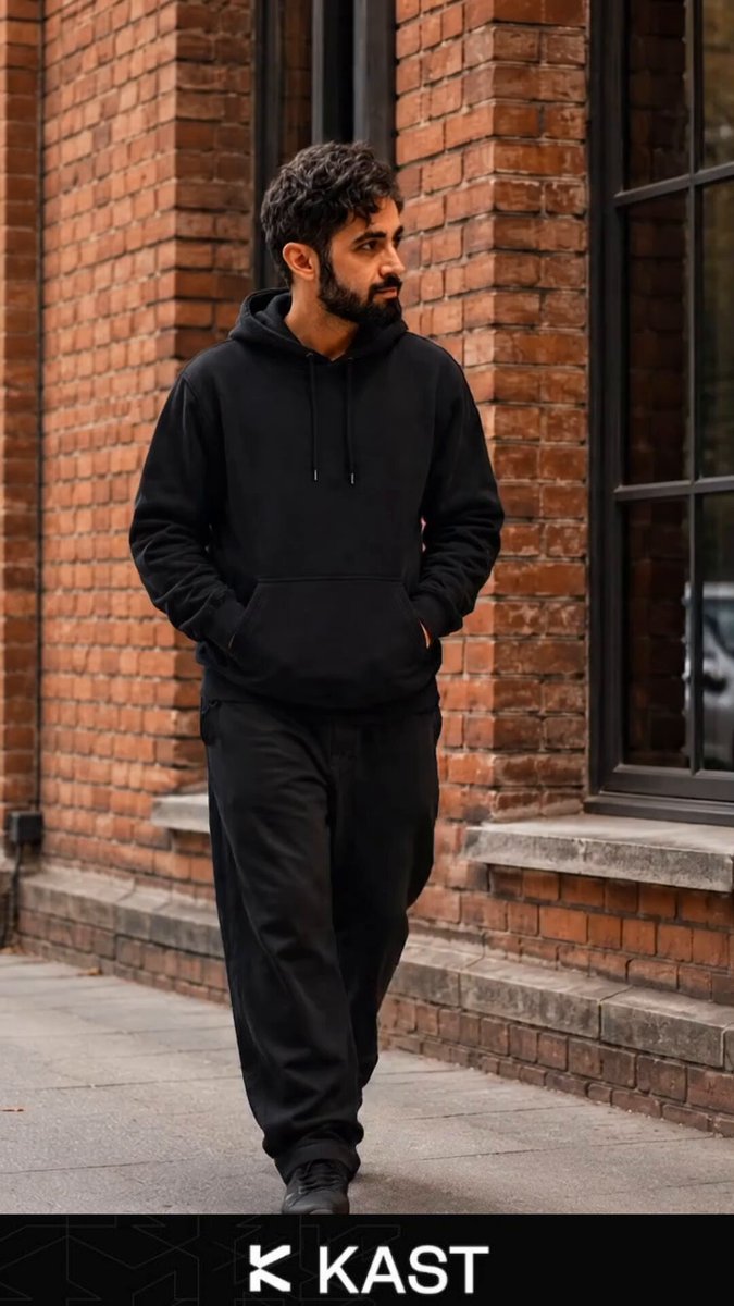 The image features a man walking down a street wearing black clothing with a hoodie over his head. The text "kast" is written above him, which could be a brand name or an event related to the photo.