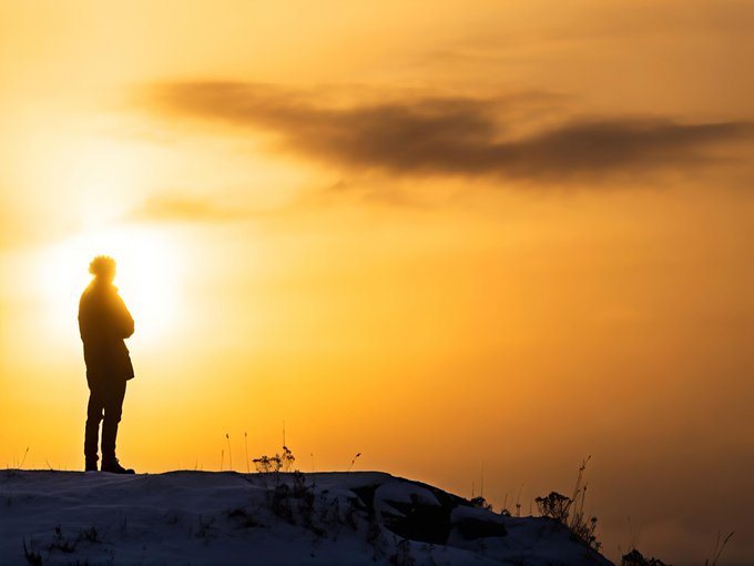 Silhouette of a person standing on a snowy hill against a golden sunset sky.