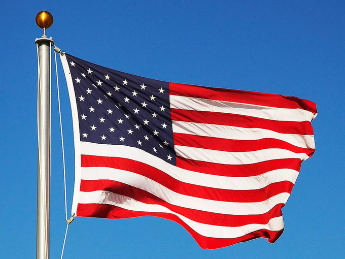 An American flag waves against a clear blue sky, symbolizing the U.S. government's significant Bitcoin holdings and its potential to shift market dynamics if it transitions from selling to accumulating BTC.