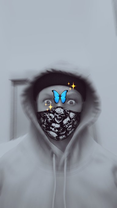 A person wearing a hooded sweatshirt, beanie, and a black-and-white patterned face mask is shown in a selfie, with a cartoon butterfly and sparkle stickers digitally added over their nose area. The image relates to the post by humorously depicting the user as a "degen" crypto investor confidently buying more BNB during a dip, trusting that CZ (Binance's founder) won't rug pull them.