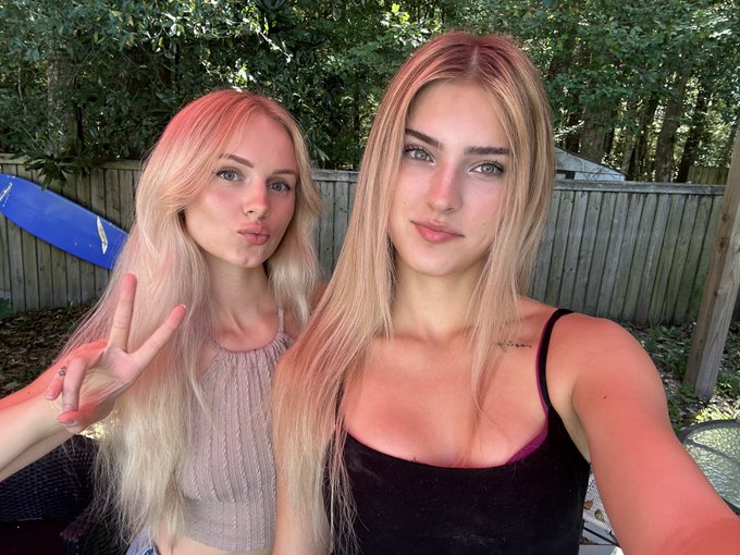Two young blonde women pose for a selfie outdoors, with one flashing a peace sign and puckering her lips while the other gazes confidently at the camera. The image captures a playful, casual moment that aligns with the post about being close to eligibility for KPP (likely "Kissing Point 7" or similar shorthand), suggesting a celebration or milestone approaching.