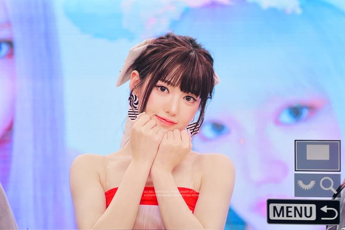A young woman with bangs, wearing a red strapless top, white bow, and zebra-print earrings, rests her chin on her clasped hands against a pastel blue and pink backdrop, with a "MENU" button visible in the corner. The post tags identify her as SUI (수이) from the group KiiiKiii (키키), dated 260814.
