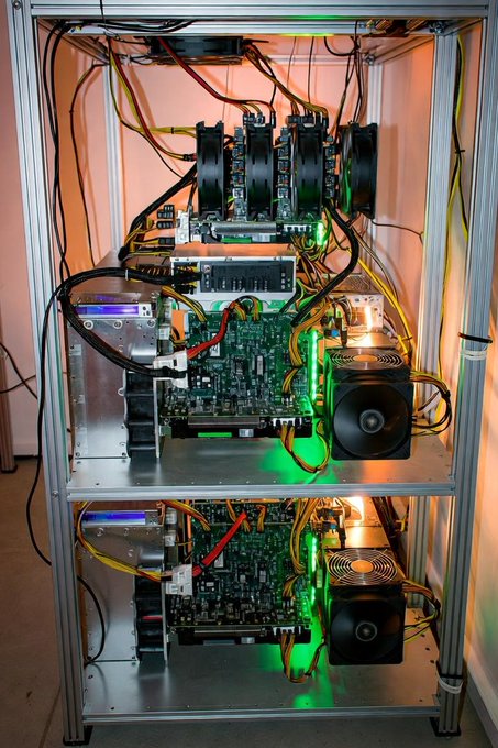 A metal shelving rack housing cryptocurrency mining equipment with exposed circuit boards, cooling fans, and numerous power cables.