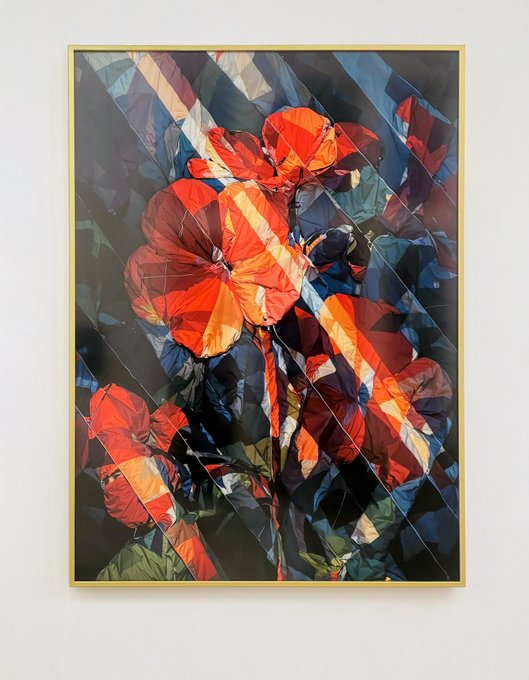 A framed abstract geometric artwork displays fragmented red floral shapes over dark, angled, stained-glass-like patterns against a plain white wall.