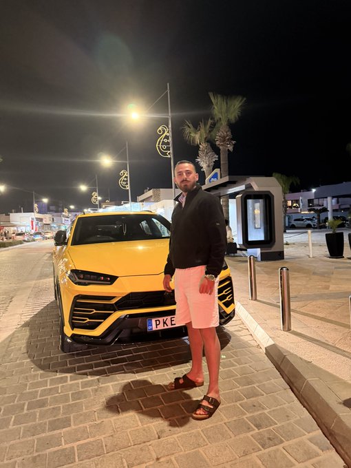 A man poses confidently beside a bright yellow Lamborghini Urus with a partially visible "PKE" license plate, captured at night in a well-lit urban setting with palm trees and street lamps. The image's luxurious, wealth-displaying aesthetic aligns with the post's "Sell gold Buy Solana" message, symbolizing the shift from traditional stores of value to crypto-driven prosperity.