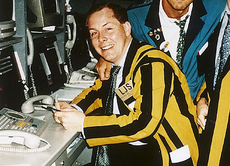 A smiling man in a yellow and black striped suit sits at a trading desk with multiple phone lines, wearing a name tag that reads "LISA." The caption contrasts the calm, friendly desk-side scene with the trader's frustration over confusing price action and suspicious TWAP activity on NEAR.