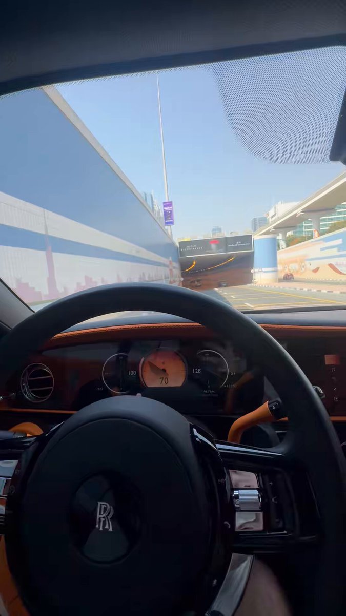 The image shows the interior of a Rolls-Royce (visible by the "RR" logo on the steering wheel) with a digital speedometer reading 70 mph, approaching a tunnel under clear blue skies. The "Billions soon" caption pairs with this view of luxury driving, suggesting success and the lifestyle that comes with it.