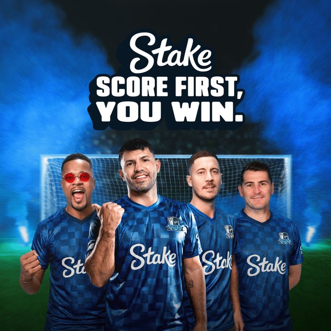 A promotional graphic for 'Stake' featuring four men in blue checkered soccer jerseys with the tagline 'SCORE FIRST, YOU WIN.'