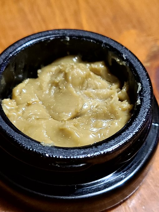 A close-up of a thick, brown paste (possibly miso or a similar spread) served in a black ceramic bowl on a wooden table.