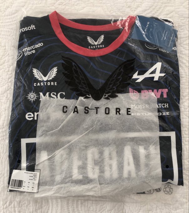 The image features a black t-shirt with white text, including the name of a company called "Casting" along with other details about the merchandise. The t-shirt has been opened, revealing its contents inside the plastic packaging. The packaging is still in good condition and appears to be intact, suggesting that it was recently unwrapped or packaged.