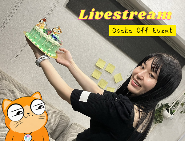 A young woman with long dark hair smiles brightly while holding up a green decorated item during a livestream, with a yellow text overlay reading "Livestream Osaka Off Event" and a cartoon orange cat sticker in the corner.