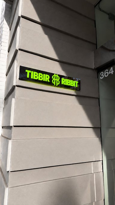 An exterior sign on a building displaying the text "TIBBIR $B RIBBIT" in glowing yellow-green letters next to the address "364".