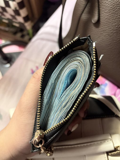 A close-up shot shows a hand holding open a black zip-around wallet, revealing it stuffed completely full of cash, emphasizing how "My wallet this September" reflects an unusually plump and overflowing state. The tightly packed bills visibly bulge at the seams, suggesting prosperity or accumulated savings from the month.