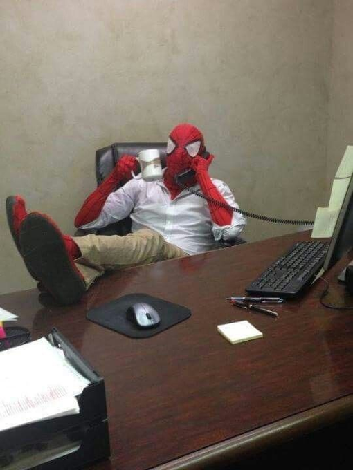 Spider-Man, wearing his costume, sits casually at an office desk with his feet up while simultaneously sipping coffee and talking on a corded telephone.