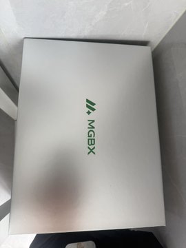 A white product box labeled 'MGBX' with a green triangular emblem on top of a desk.