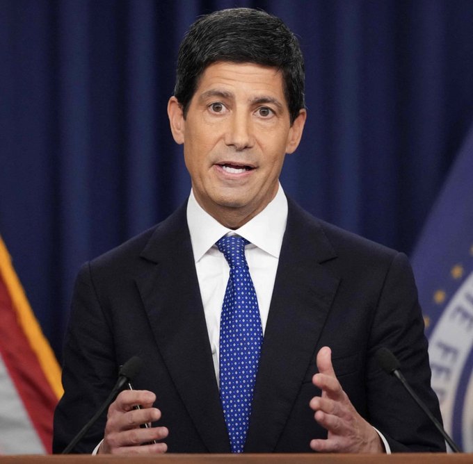 Kevin Warsh speaks at a podium in a dark suit and blue tie, with U.S. and institutional flags behind him. The image accompanies his statement that “Inflation is too high,” signaling that interest-rate cuts may not come soon and putting pressure on Bitcoin near $78.2K–$75.9K.