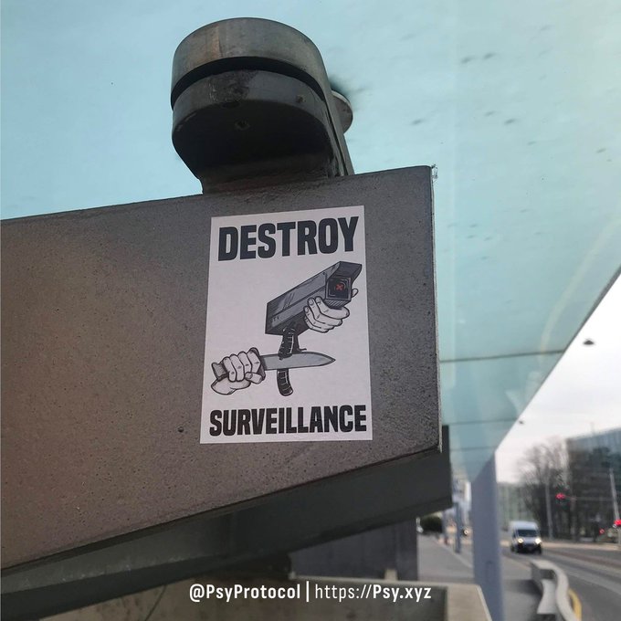 A sticker reading "DESTROY SURVEILLANCE" depicts hands using a knife to cut through a surveillance camera, affixed beneath an actual security camera. The image powerfully illustrates the post's point about the false equivalence between blockchain transparency and privacy, as on-chain data—despite being "public"—creates a permanent, analyzable surveillance record of every wallet and transaction, ironically trading privacy for openness.