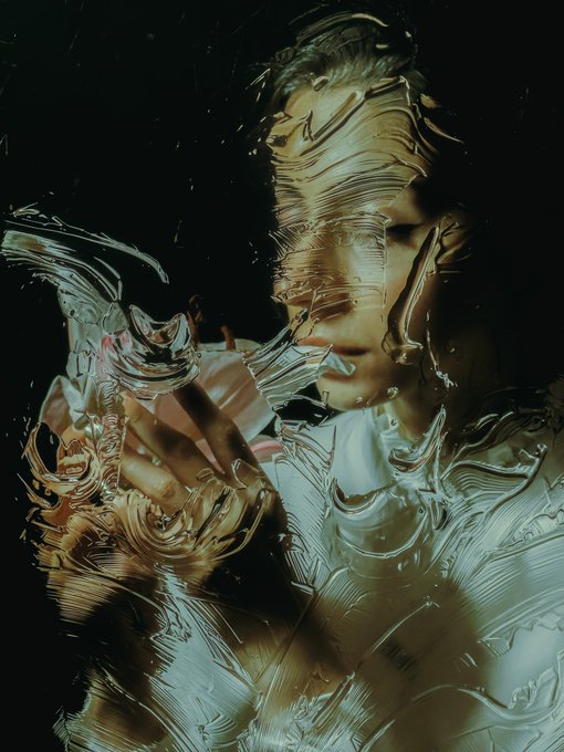 A highly distorted, abstract portrait of a person whose face and body appear to be melting or viewed through rippled, liquid-like glass against a dark background.