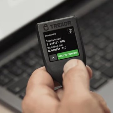 A hand holding a Trezor hardware wallet displaying a summary screen for a Bitcoin transaction showing a total amount of 0.203121 BTC and a fee of 0.000551 BTC.