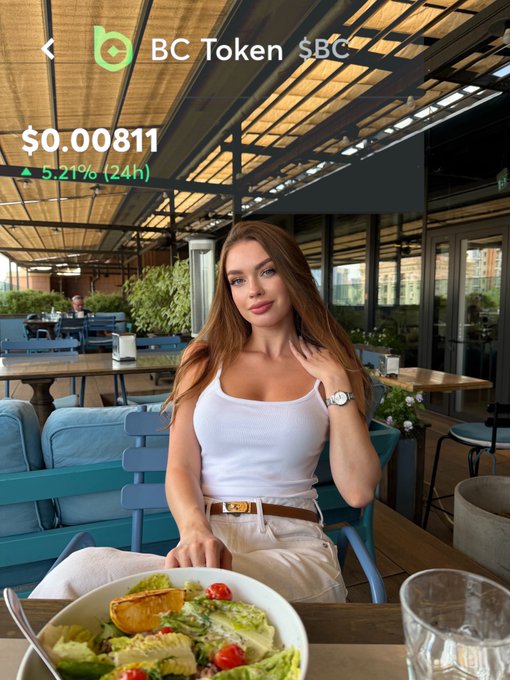 The image shows a woman sitting at an outdoor restaurant table, enjoying her meal consisting of a bowl of food placed in front of her. The scene also includes several chairs around the dining tables, as well as potted plants adding greenery to the area. A cup can be seen on one of the tables nearby.
