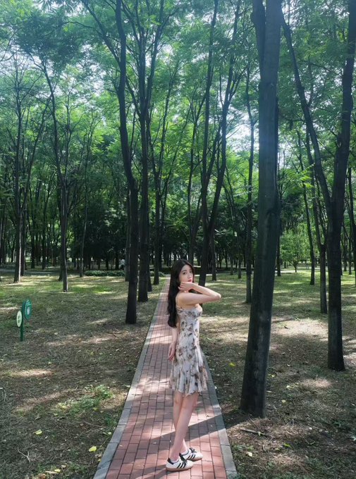 A woman in a floral dress poses on a brick pathway through a lush green forest.