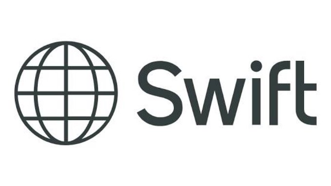 The image shows the Swift logo, featuring a wireframe globe icon next to the company name "Swift" in bold gray lettering. This relates to the news of Swift's new blockchain-based payment infrastructure, as the logo represents the company leading the initiative with 17 global banks preparing to pilot tokenized cross-border transactions.