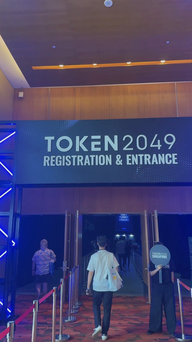 Photo of the entrance to TOKEN2049 in Singapore, showing attendees walking into the conference registration area.