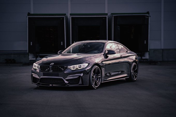 A sleek, dark-colored BMW sports coupe parked in front of a building with open loading dock doors.